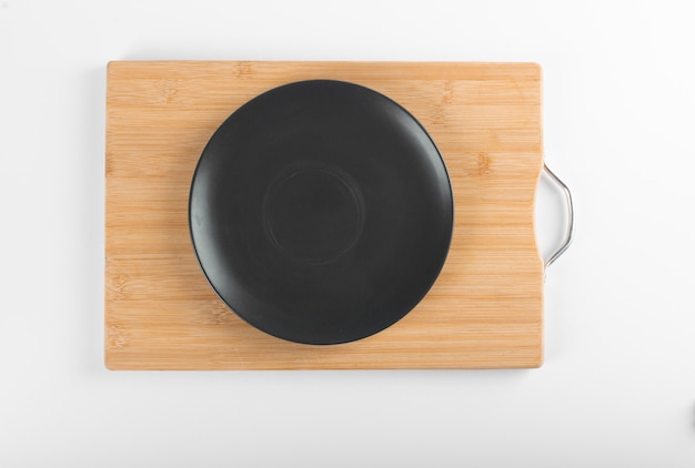 An empty black saucer on a wooden board