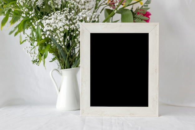 Empty blank photo frame with flower vase on white table