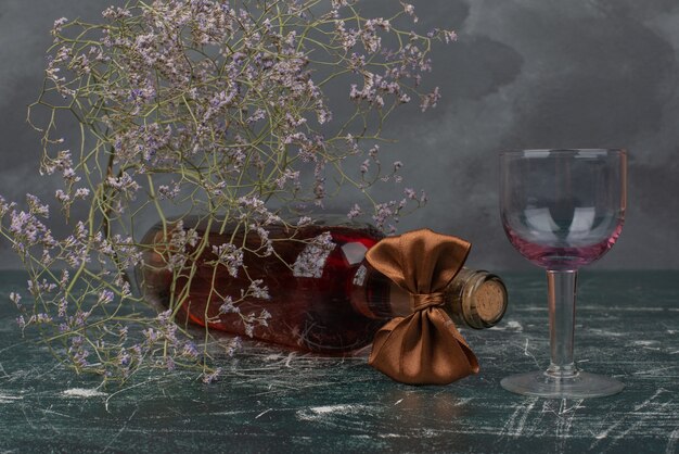 Empty bottle and glass with withered flower on marble surface . 