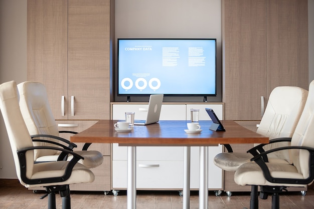 Empty business meeting conference room with graphs and diagrams on TV in the background