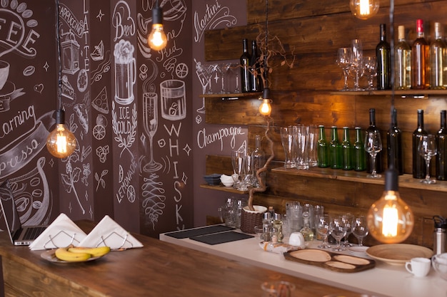 Empty cafe bar interior design with artistic drawing in the back. Wine bottles . Light bulbs hanging from the ceiling.