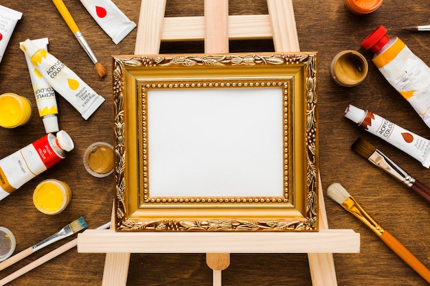 Empty canvas in golden frame and paint flat lay