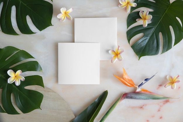 Empty card with envelope on marble table and tropical flowers.