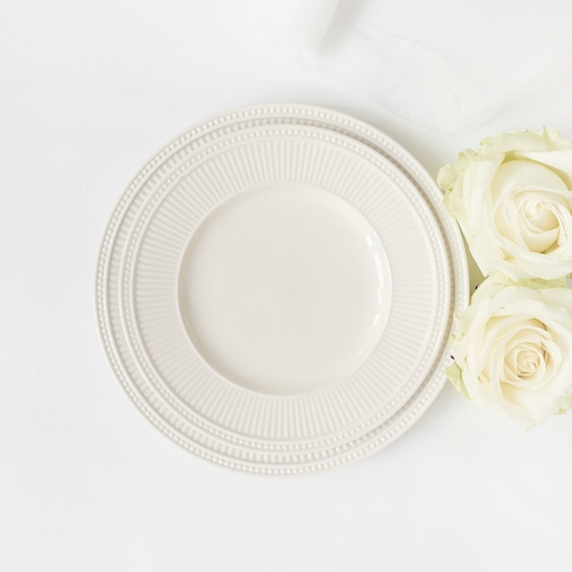 Free photo an empty ceramic plate and roses on white background