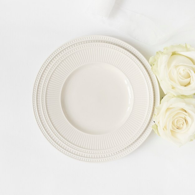 An empty ceramic plate and roses on white background
