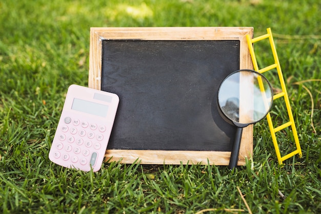 電卓と草の上の拡大鏡を持つ空の黒板