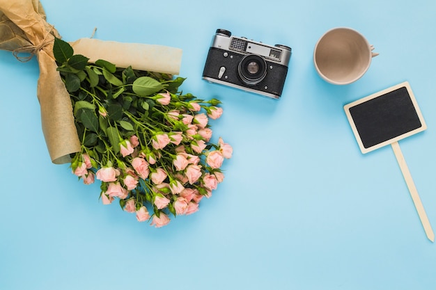 빈 컵; 카메라; 핑크 장미 꽃다발과 파란색 배경에 빈 레이블