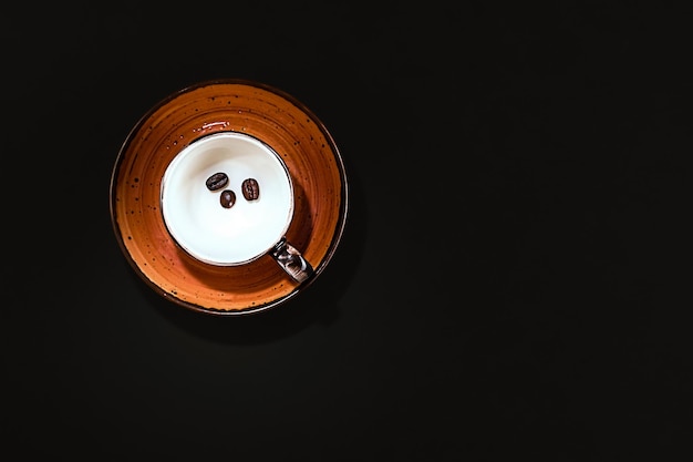 Empty espresso coffee cup with coffee beans in a mug on a black color background top view Minimalist breakfast idea table setting coffee lovers