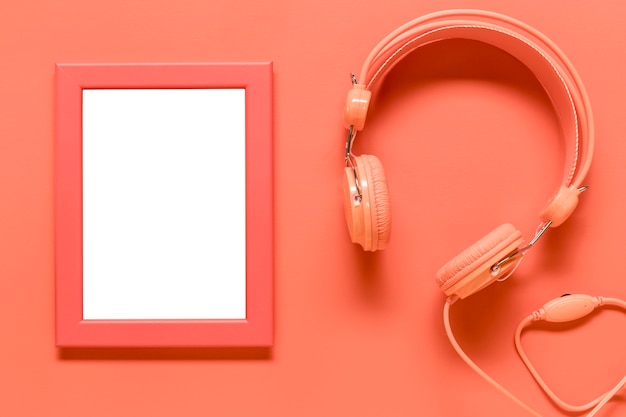 Empty frame and pink earphones on colored surface