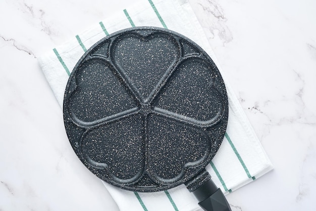 검은색 빈 프라이팬, 석재 논스틱 코팅이 된 프라이팬은 아침 식사 하트 모양으로 팬케이크를 굽고 회색 콘크리트 테이블 배경에 재료를 넣습니다. 발렌타인 데이를 위한 아침 식사. 평면도. 프리미엄 사진