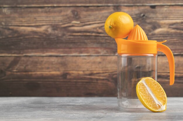 An empty glass pitcher with a one whole lemon on a wooden.