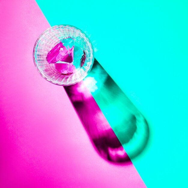 An empty glass with shadow on dual pink and turquoise background