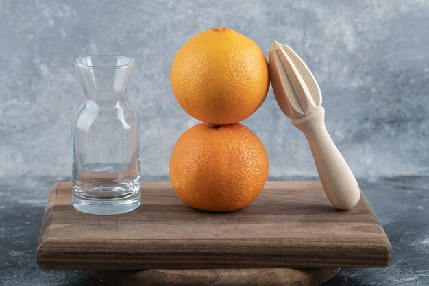 Пустой стакан, деревянная развертка и апельсины на деревянной доске.