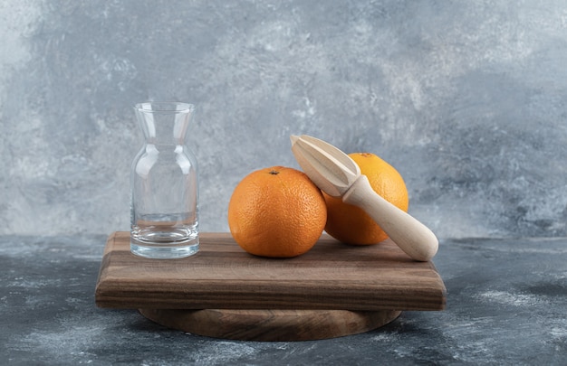 Empty glass, wooden reamer and oranges on wooden board. 