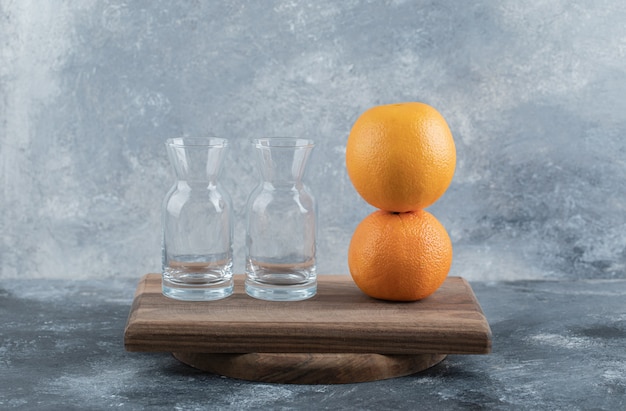 Empty glasses and ripe oranges on wooden board.