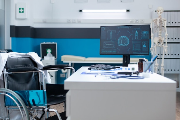 Empty modern hospital office room equipped with medical professional equipment ready for patient consultation. Computer standing on table having human body skeleton on screen. Medicine concept