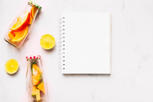 Empty notebook lime and glass bottles with cut ​​citrus