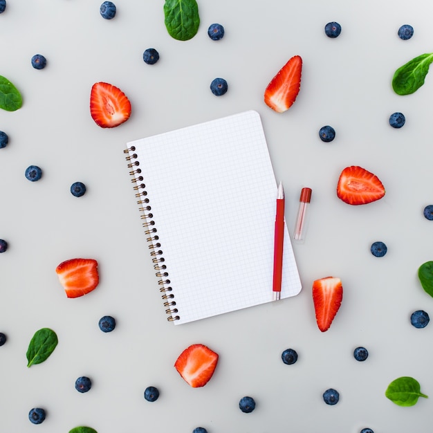 Empty notebook with strawberries and blueberries on grey background