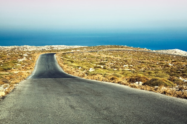 ギリシャの地中海沿岸に向かって走る空の舗装道路-旅のコンセプト