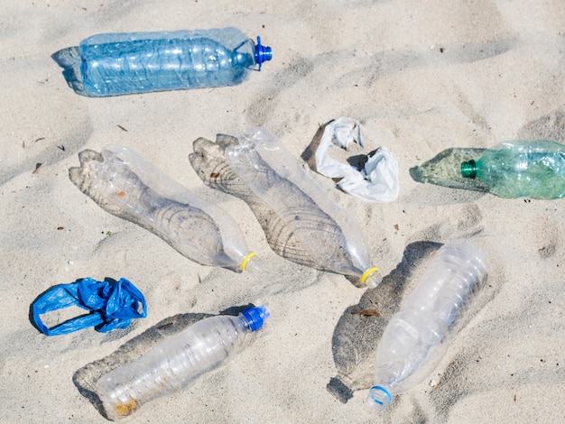 Foto gratuita svuoti le bottiglie di acqua di plastica e il sacchetto di plastica sulla sabbia