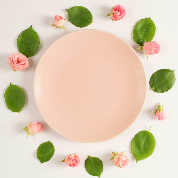 Free photo empty plate surrounded by beautiful pink flower and leaves arranged in circular frame