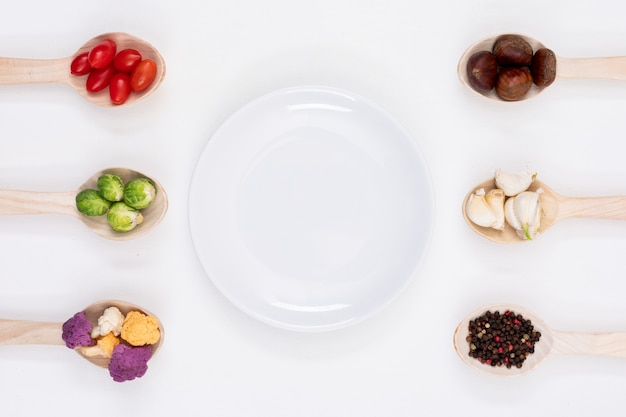 Free photo empty plate surrounded by vegetables in the wood spoons on white