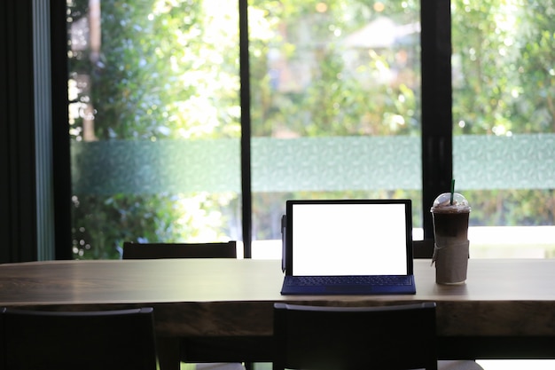 Пустой экран ноутбука и кружка холодного кофе, помещенный на стол для еды в кафе.