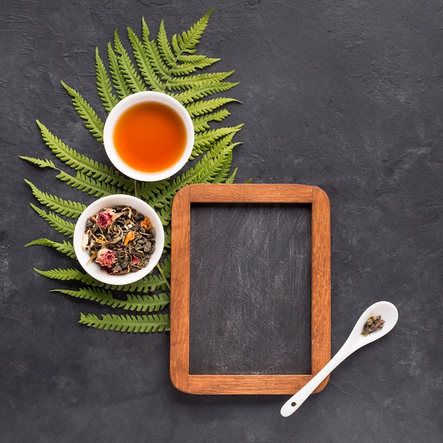 Empty slate with dry leaves and tea in ceramic bowl on black textured background