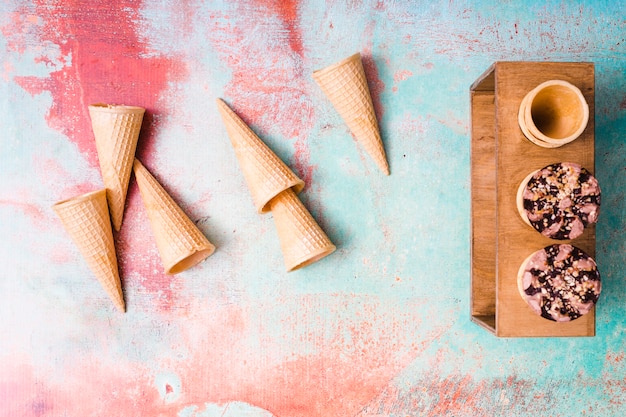 Free photo empty waffle cones and chocolate ice cream in cups on multicolored background