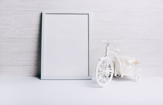 An empty white frame near the bicycle on white desk against wooden wall