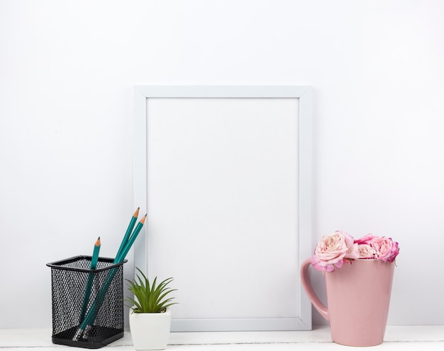 Empty white frame; pencil stand; flowers and succulent plant on table