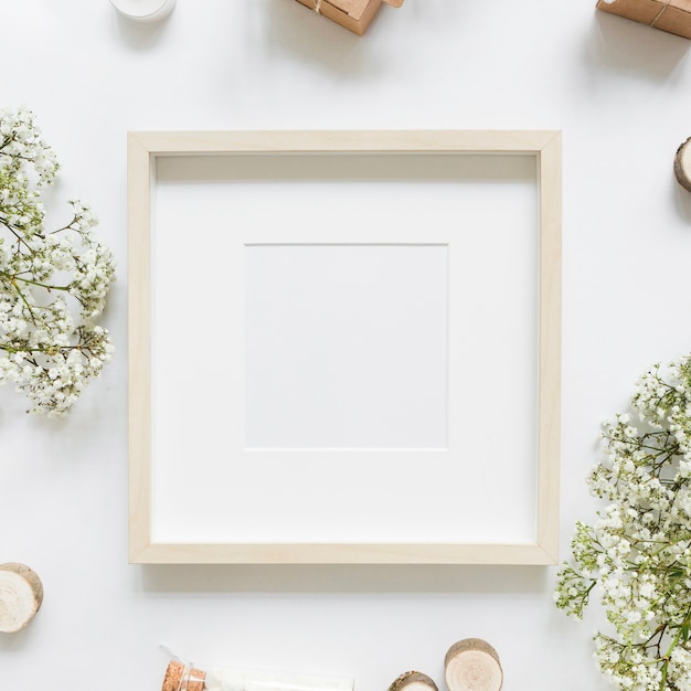 An empty white frame surrounded with flowers and gift boxes