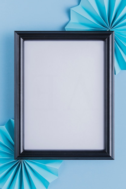 Empty white picture frame and origami fan over blue backdrop