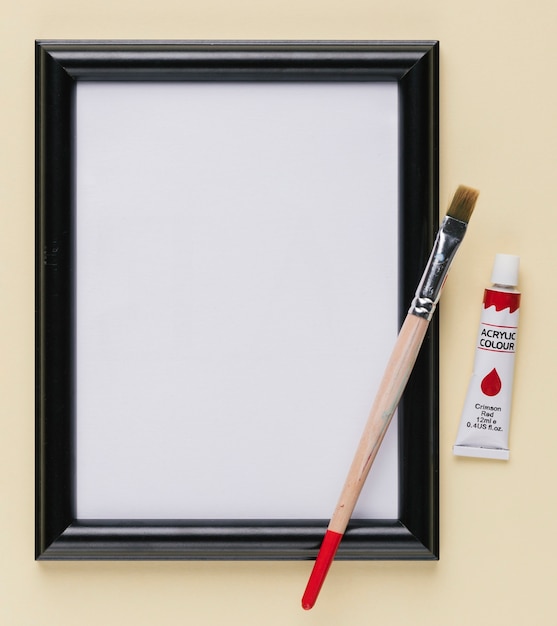 Empty white picture frame with paint tube and paintbrush
