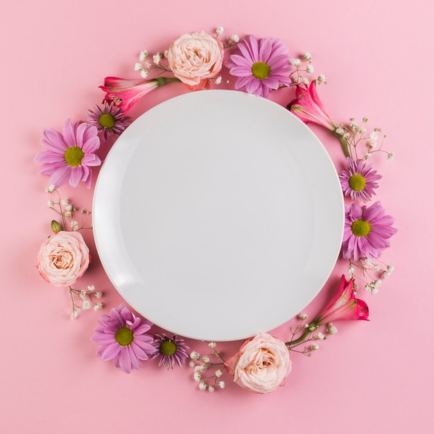 An empty white plate decorated with colorful flowers against pink background