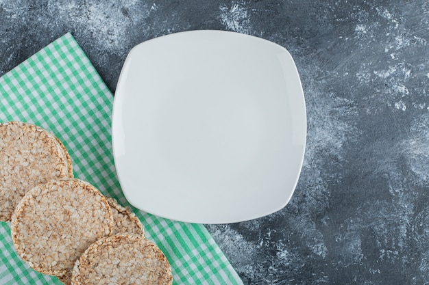 Un piatto bianco vuoto con pane di riso croccante su una superficie di marmo.