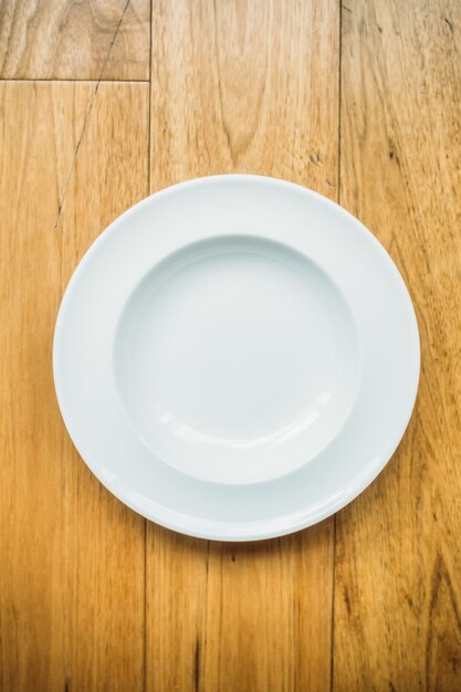 Пустая белая тарелка на деревянном фоне