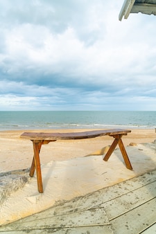 海​の​ビーチ​の​背景​を​持つ​ビーチ​の​空​の​木製​ベンチ