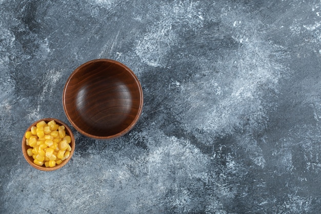 An empty wooden bowl with small bowl of popcorn seeds.