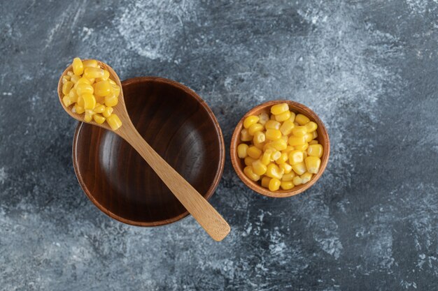 An empty wooden bowl with a wooden spoon of popcorn seeds.
