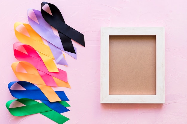 An empty wooden frame with colorful awareness ribbon on pink background