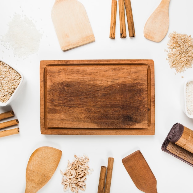 Empty wooden tray with spatula; rice; cinnamon sticks on white background