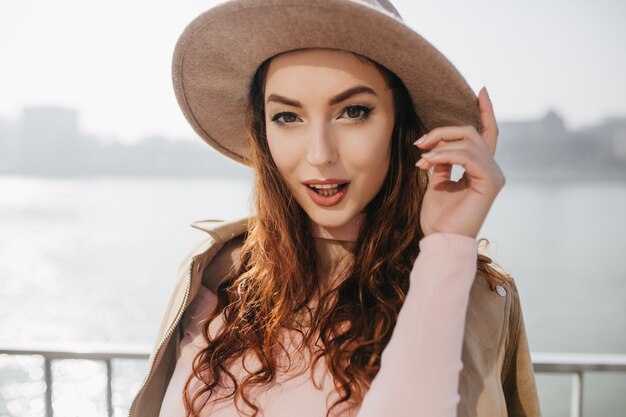 Enchanting brown-haired woman playfully posing on river wall