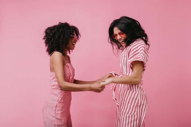 Free photo enchanting girls joking together while posing. pretty african woman holding hands with friend and dancing.