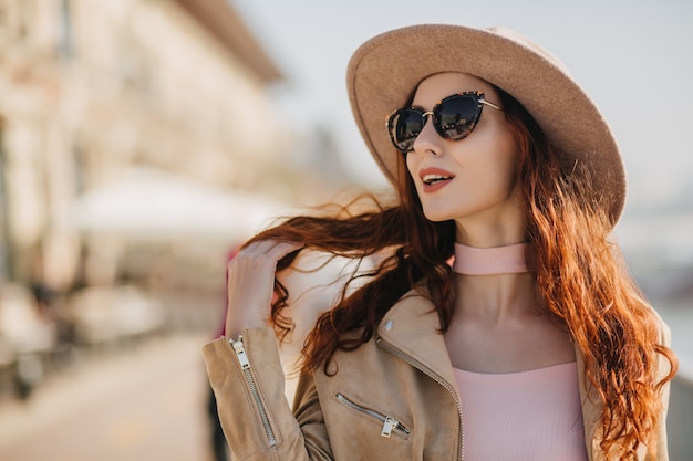 Enchanting red-haired woman in elegant sunglasses dreamy looking away