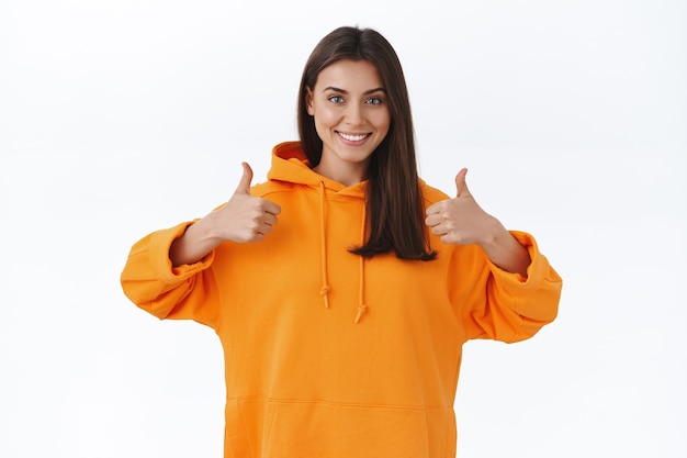 Encouraging and supportive charming brunette woman with beaming smile, showing thumbs-up in approval, like or accept gesture, praise nice job, saying well done