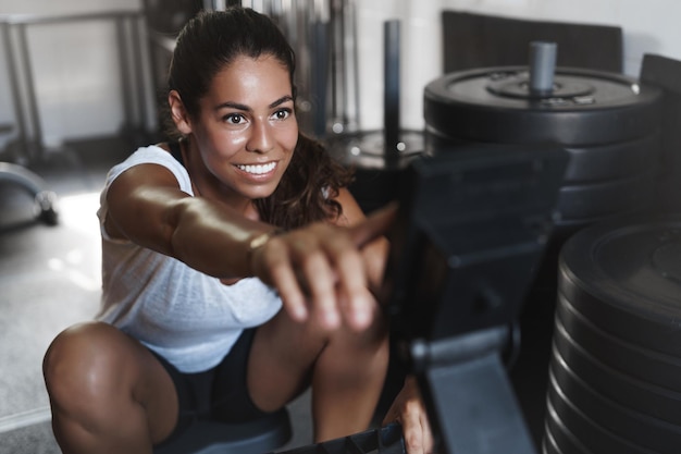 Endurance workout and fitness concept Happy and motivated woman with sweat on face program equipment during training session smiling delighted pushing weight with legs as using leg press