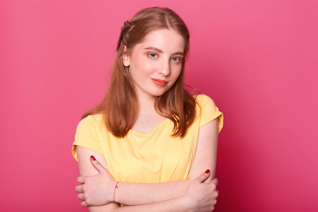 Energetic positive model poses wearing light yellow casual t shirt with cute facial expression, brown toned makeup and hairdo, looks confident and sweet. Youth, leisure and emotions concept.