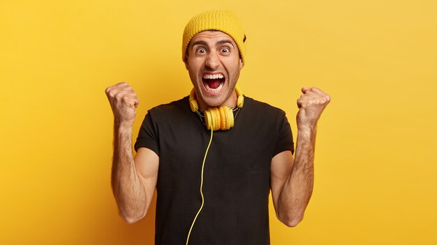 Energized man shouts loudly, clenches fists, has fun indoor