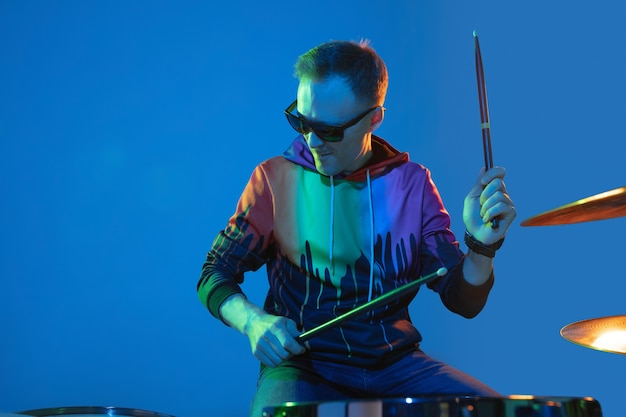 Free photo energy. young inspired and expressive musician, drummer performing on gradient colored wall in neon light. concept of music, hobby, festival, art. joyful artist, colorful, bright portrait.